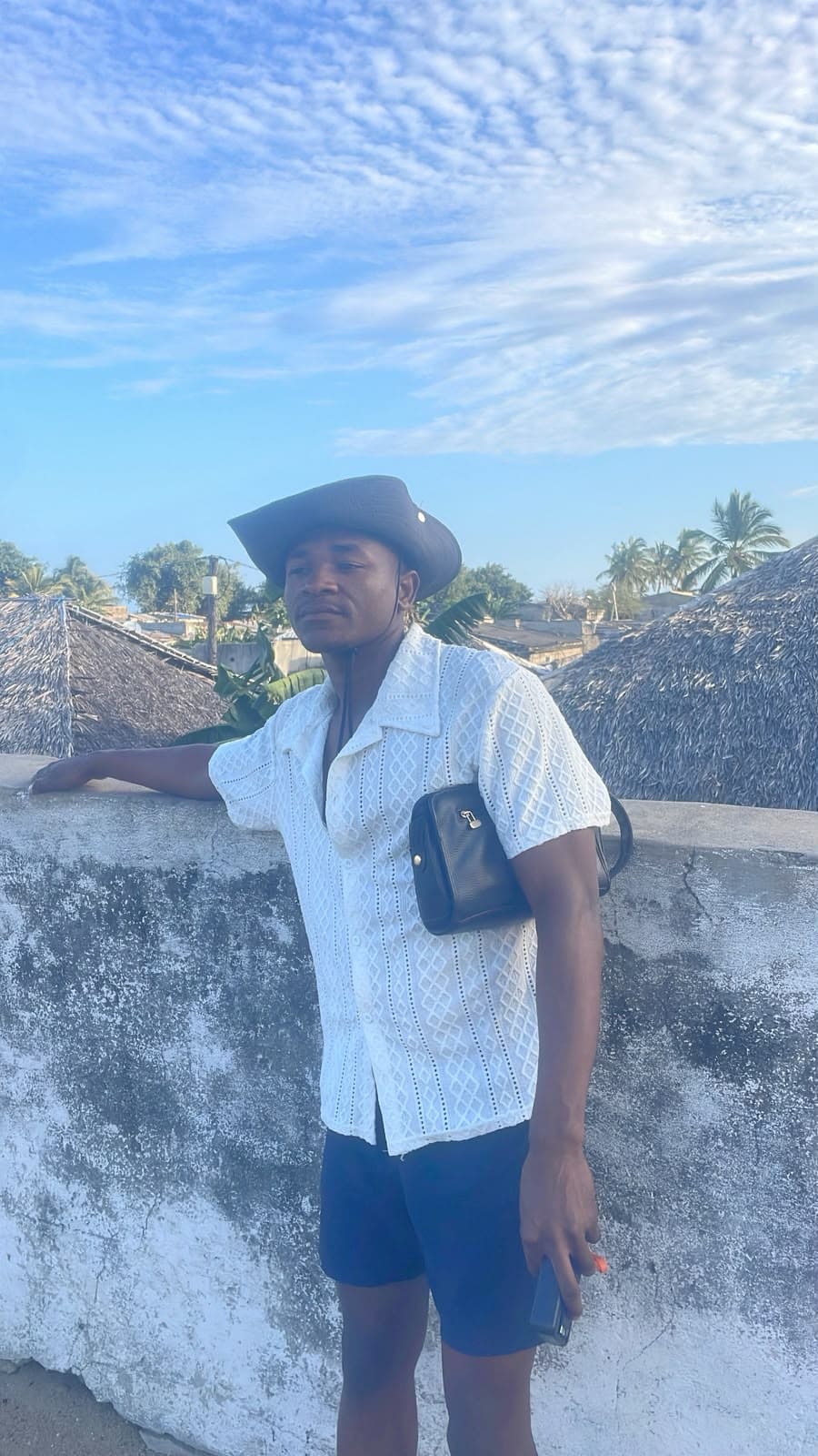 Michael de chapéu, encostado num muro, sob um céu aberto em Moçambique